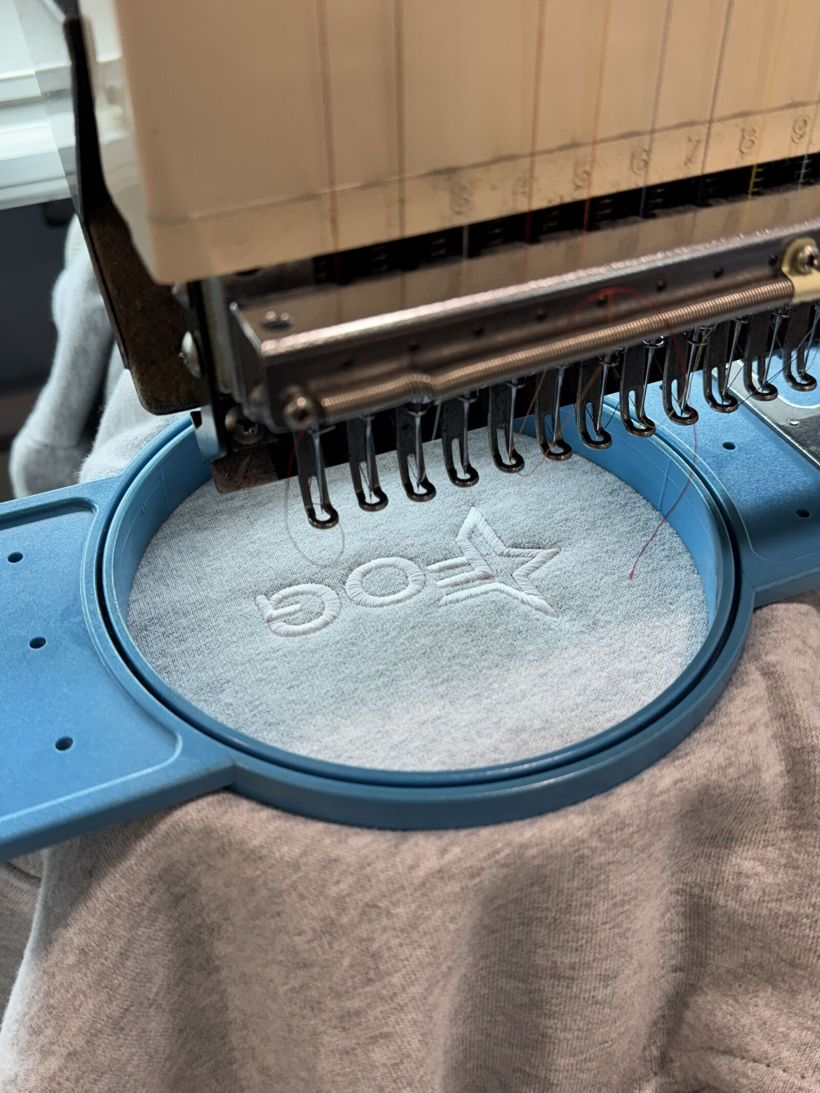 Embroidery machine hoop stitching white logo onto heather grey sweatshirt