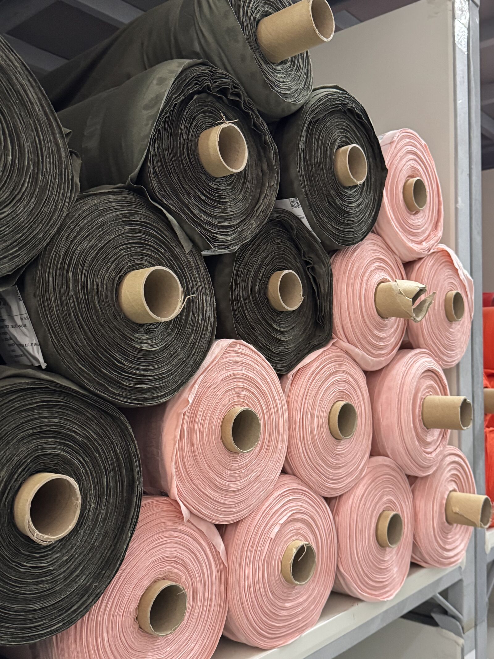 Stacks of fabric rolls in pink and charcoal on factory shelving