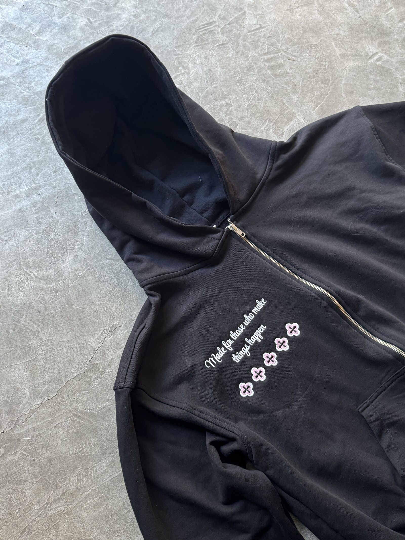 Black zip-up hoodie with white embroidered script and pink flower patches